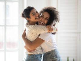 Happy multiethnic girlfriends have fun hugging indoors