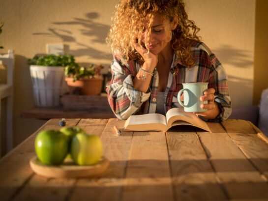 Beautiful curly adult woman read a book outdoor at home enjoying a book